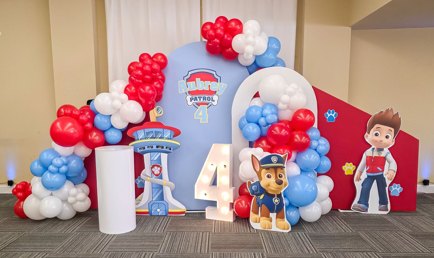 Paw Patrol-themed birthday display with balloon arch, a Chase cutout, and the number 4. Red, blue, and white colors.