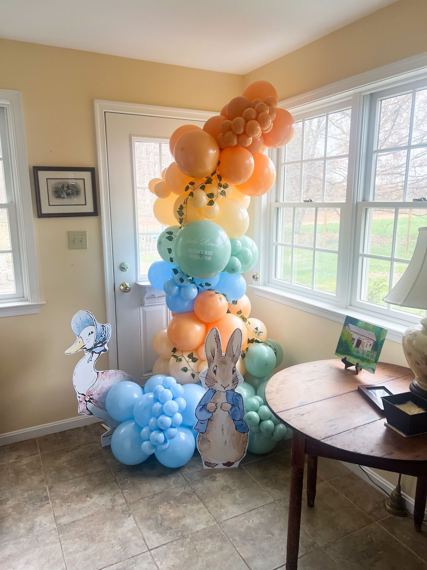 Balloons in shades of orange, blue, and green decorate for a party, with a Peter Rabbit prop.