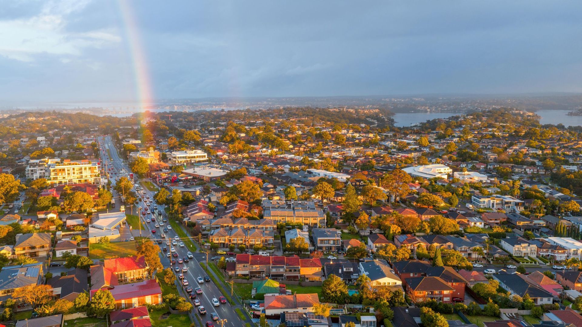 Aerial view of a colorful suburban neighborhood with a rainbow and a distant waterfront at sunset