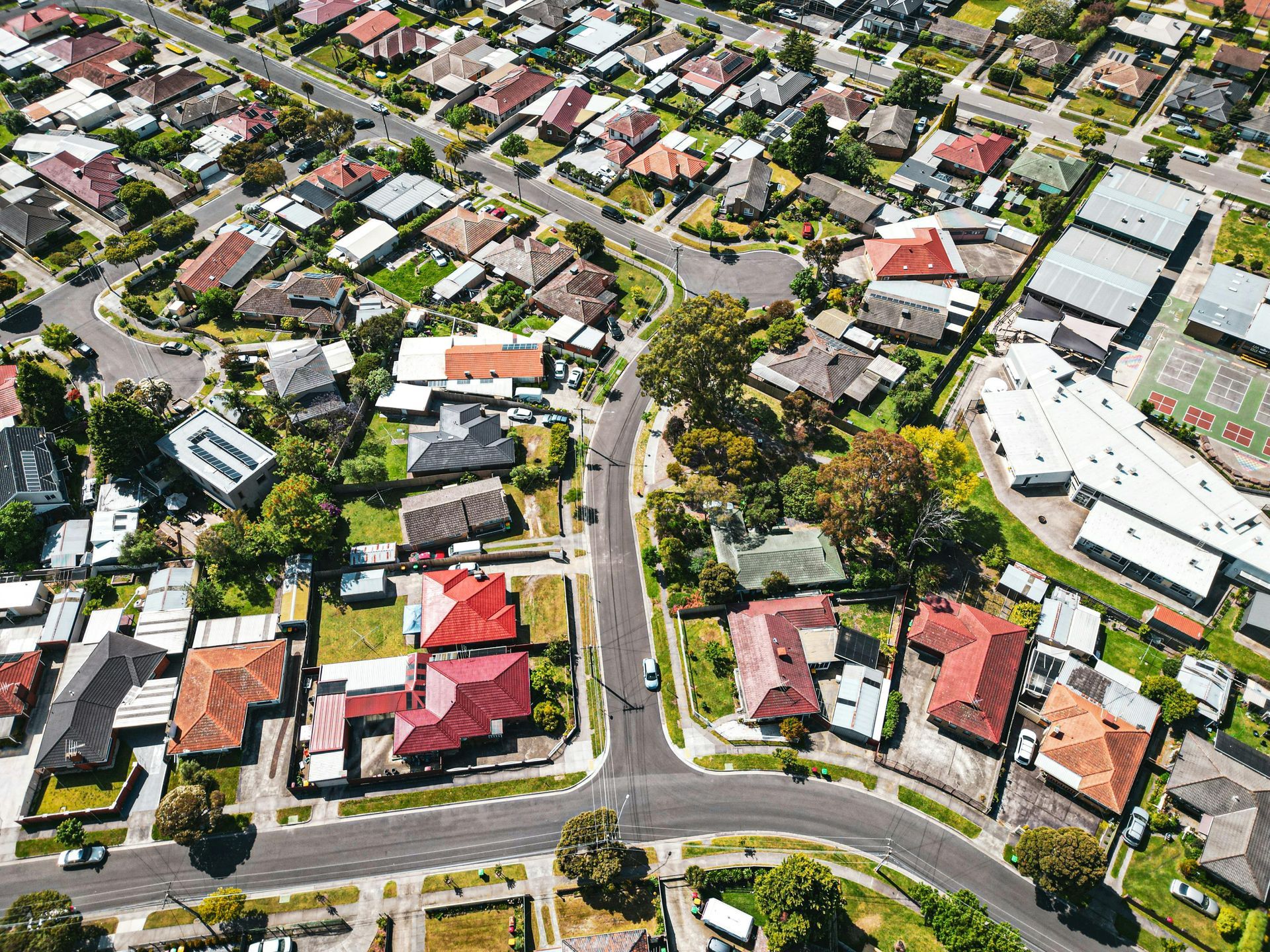 Aerial view of a suburban neighborhood with houses, roads, and trees on a sunny day