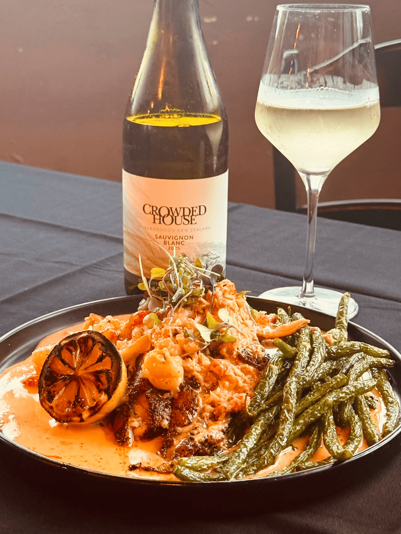 Plated seafood pasta with herbs, lemon, and wine bottle and glass on an outdoor table