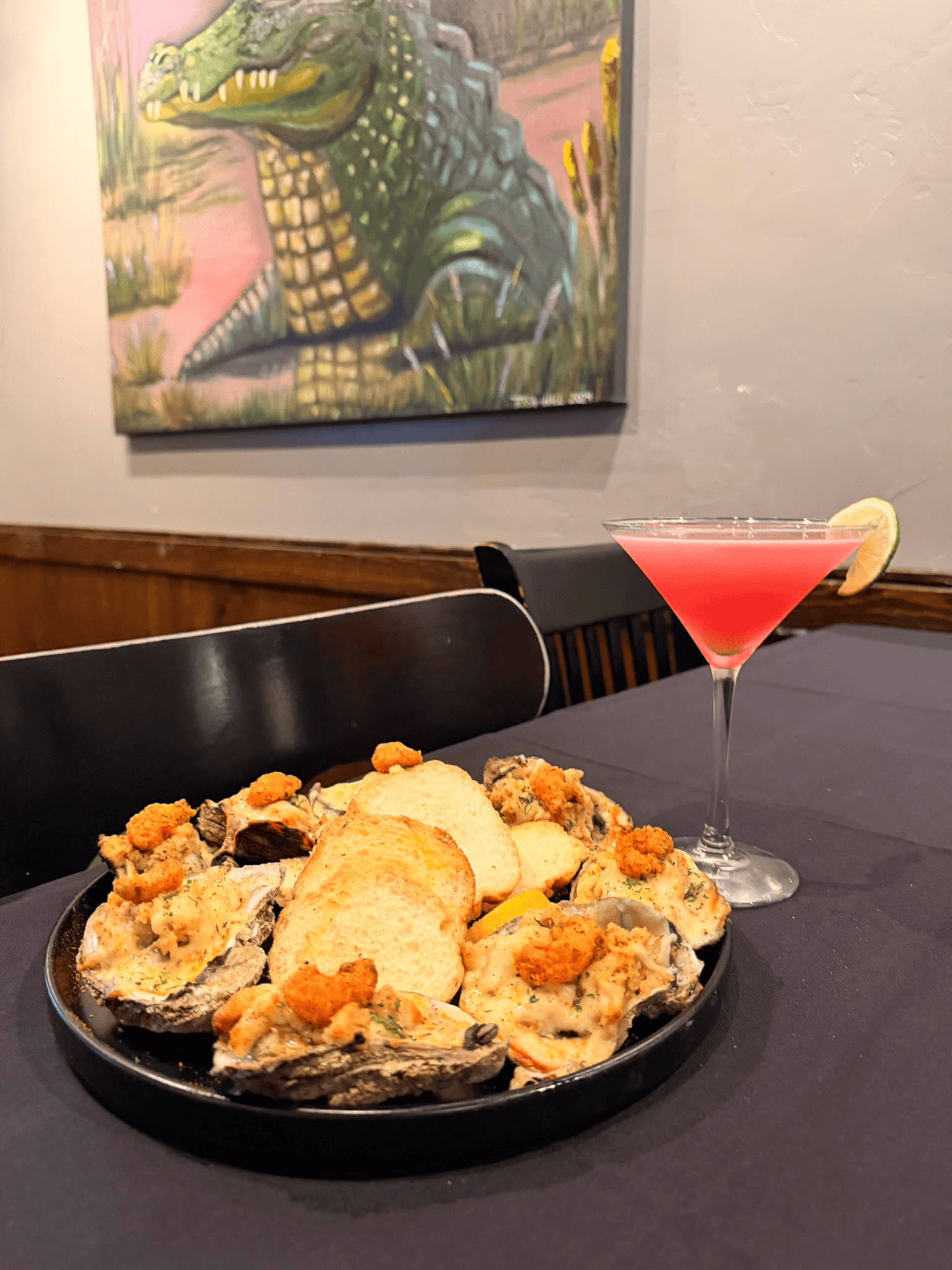 Tabletop plate of fried food with dipping sauce beside a pink cocktail in a restaurant booth.