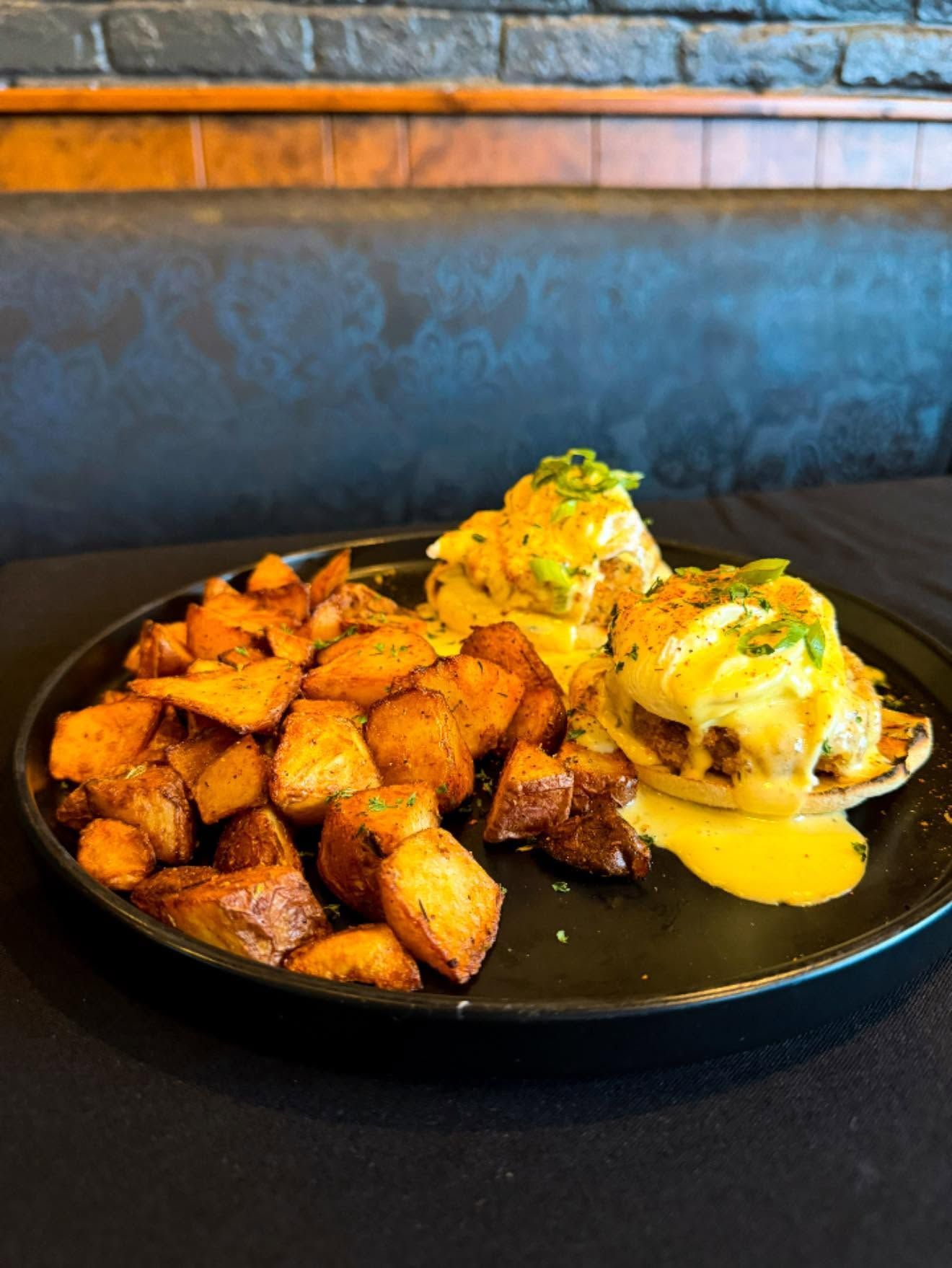Black plate with roasted potatoes and eggs benedict on a dark table in a restaurant setting