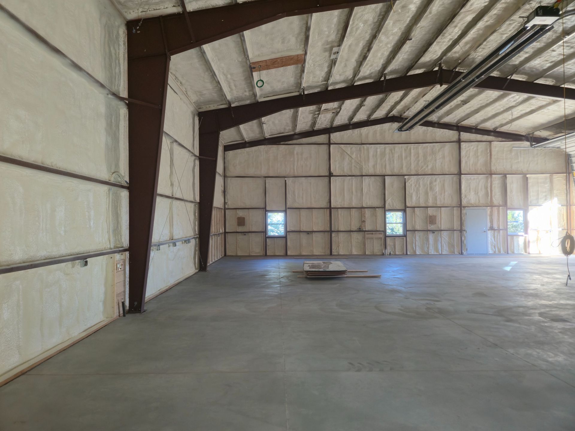 Empty warehouse interior with concrete floor, metal roof beams, and a small central pallet.