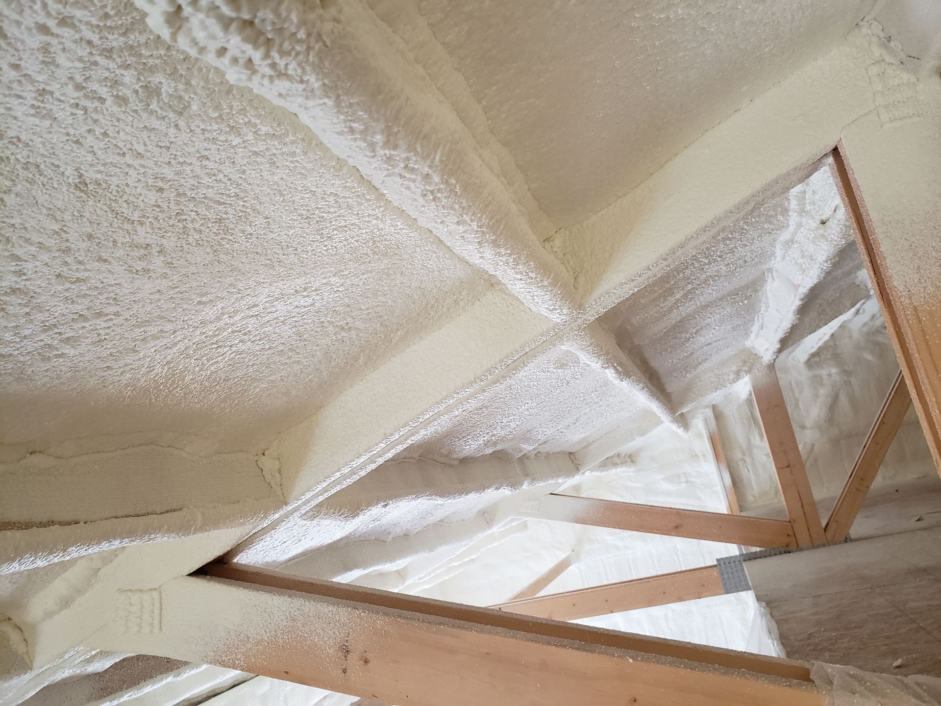 Attic interior with spray foam insulation on rafters and ceiling. White and light tan colors.