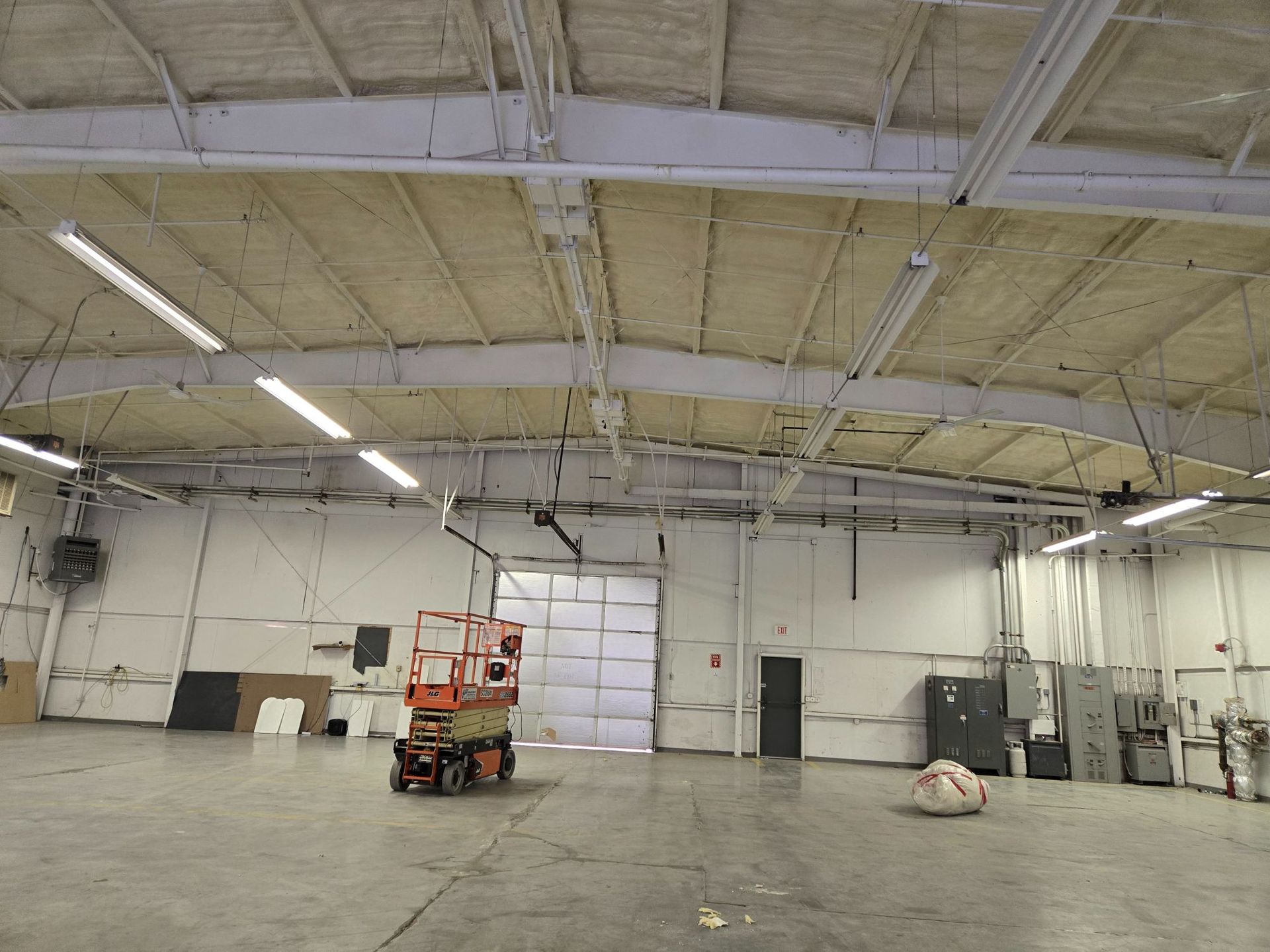 Empty warehouse interior with high ceiling, a lift near center, and a large white rolling door.