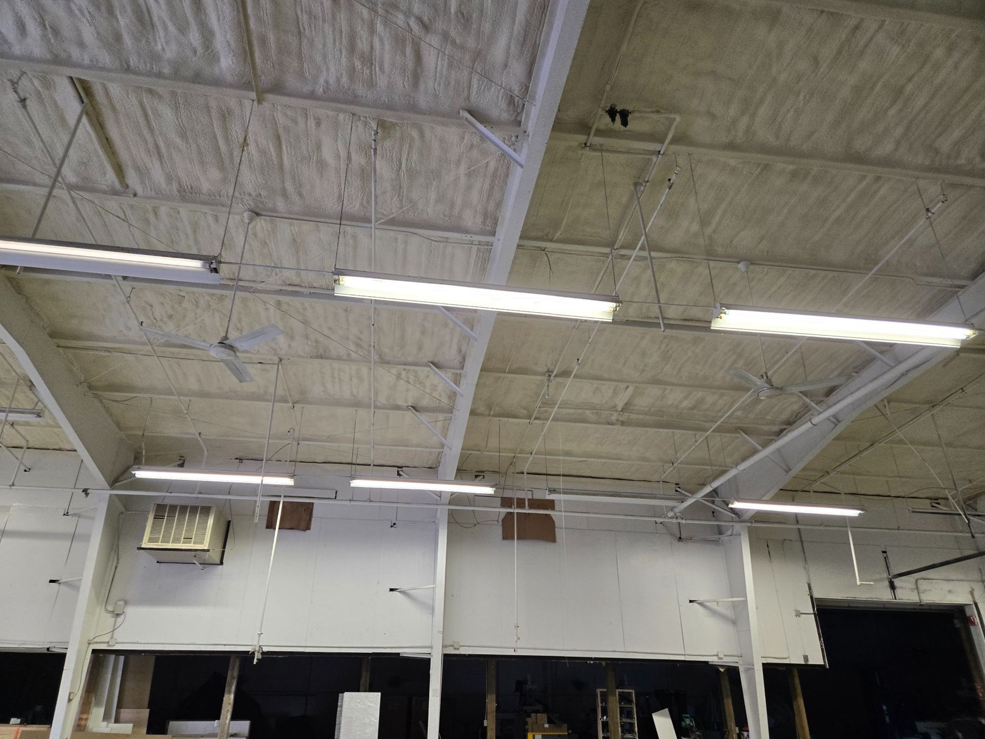 Industrial warehouse ceiling with fluorescent lights, white beams, and insulated panels above loading bays