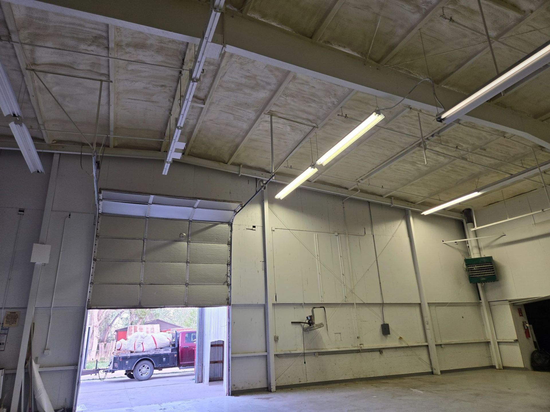 Empty industrial garage interior with a raised roll-up door and fluorescent ceiling lights.