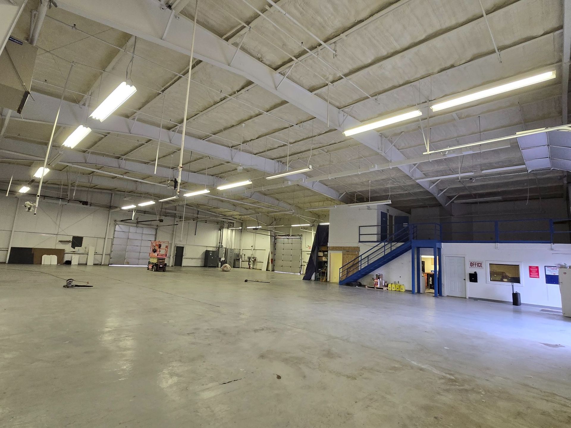 Empty warehouse interior with high ceiling, concrete floor, and a blue staircase on the right