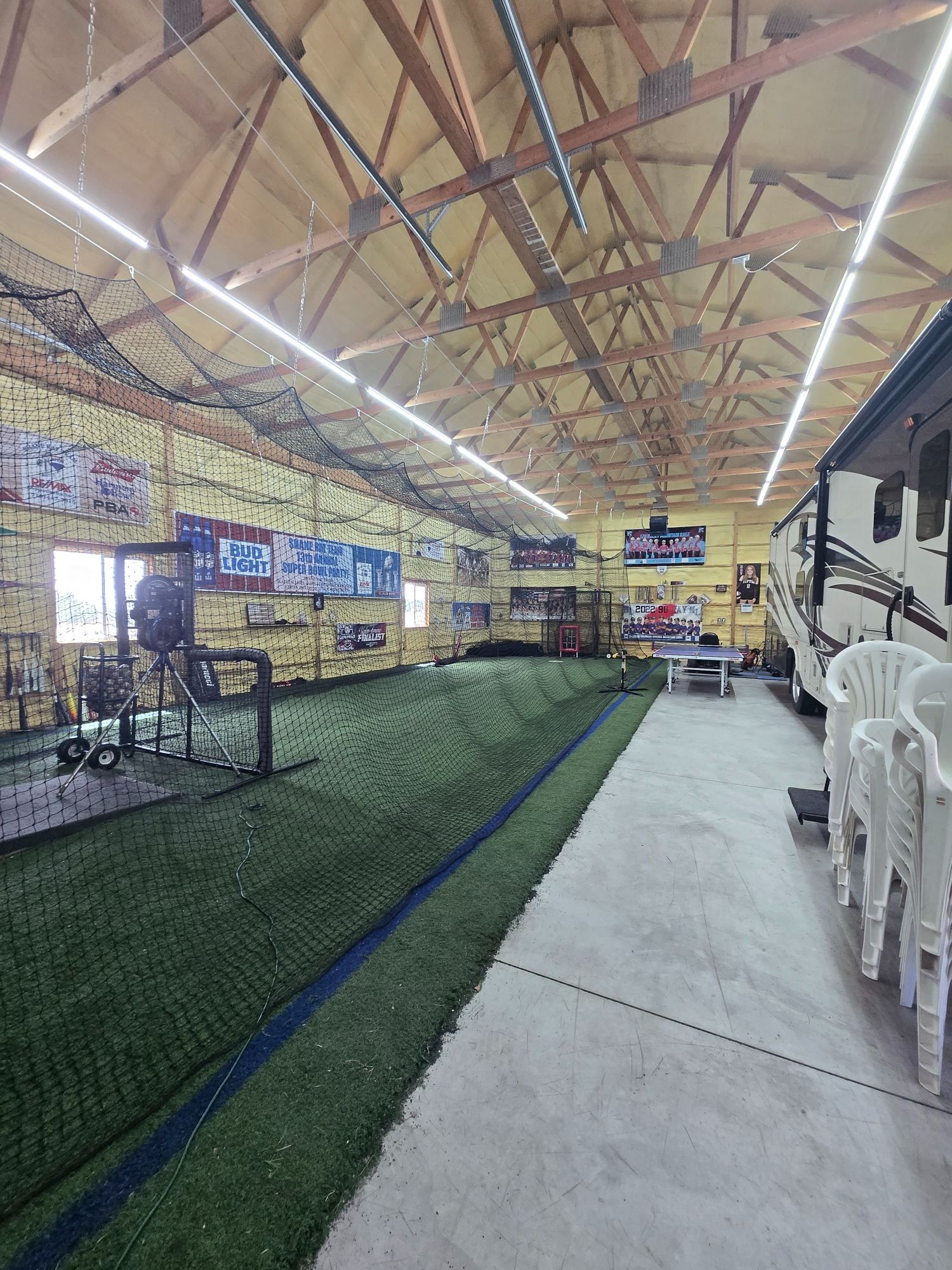 Indoor market aisle with green turf and concrete walkway under a wooden roof, lined with stalls and seating.