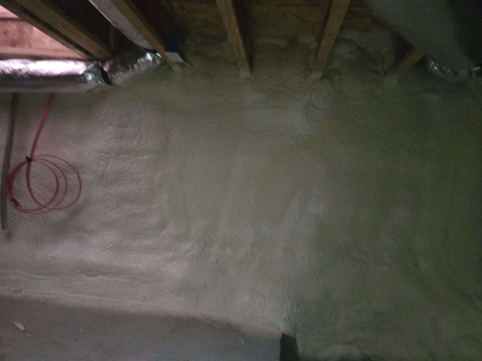 Partially finished attic with exposed rafters, white insulated floor, and red cable loop on the left