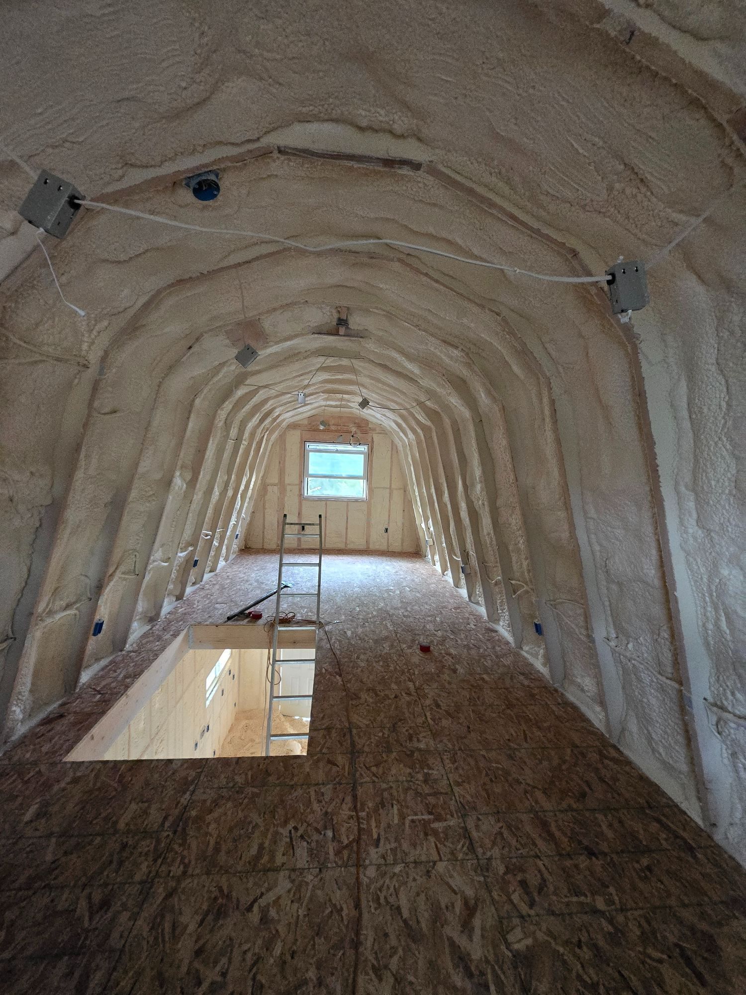 Attic interior filled with loose, light-colored insulation; wooden beams and rafters support the roof.