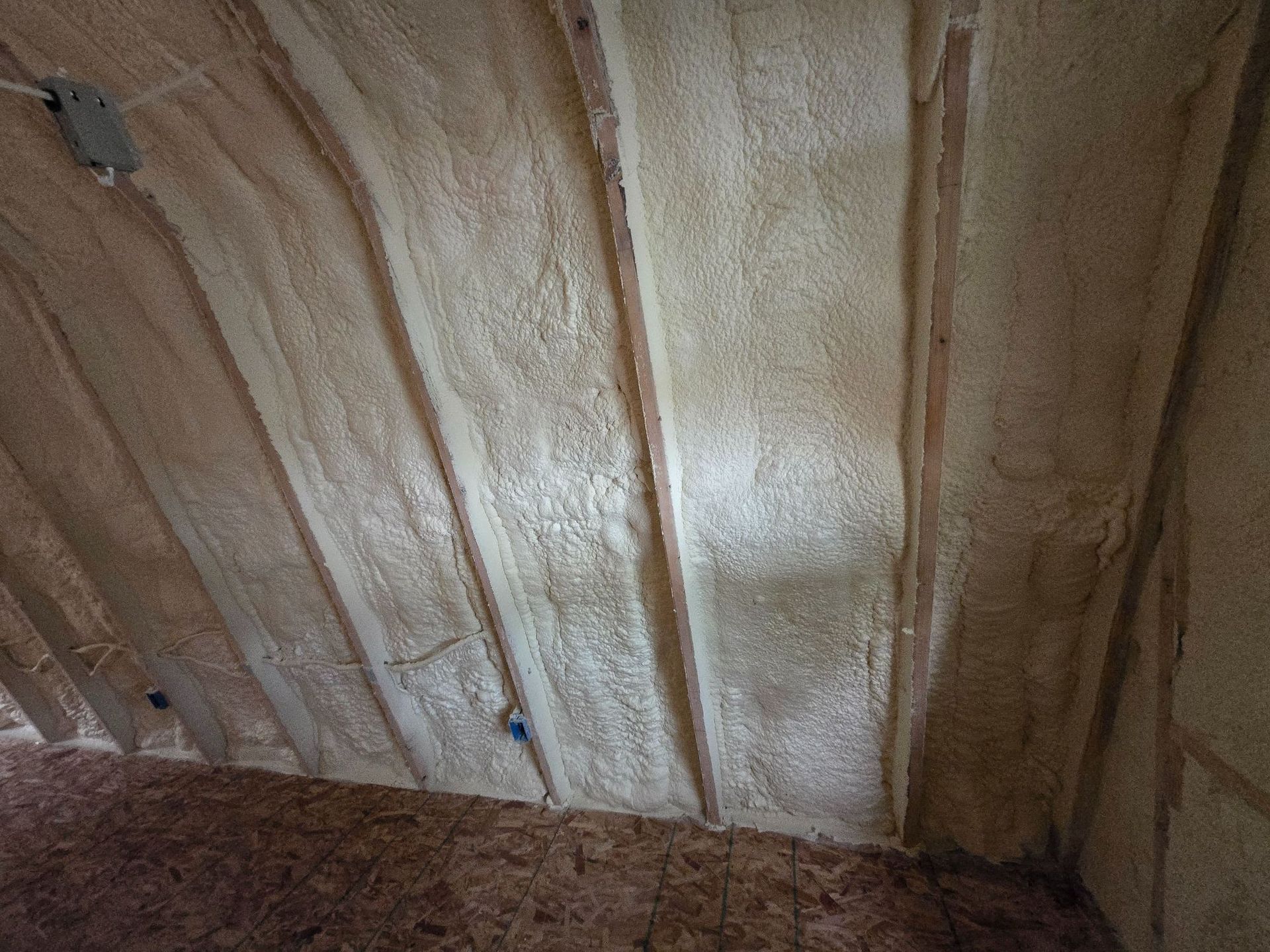 Close-up of insulated wall studs with beige foam and exposed wood framing