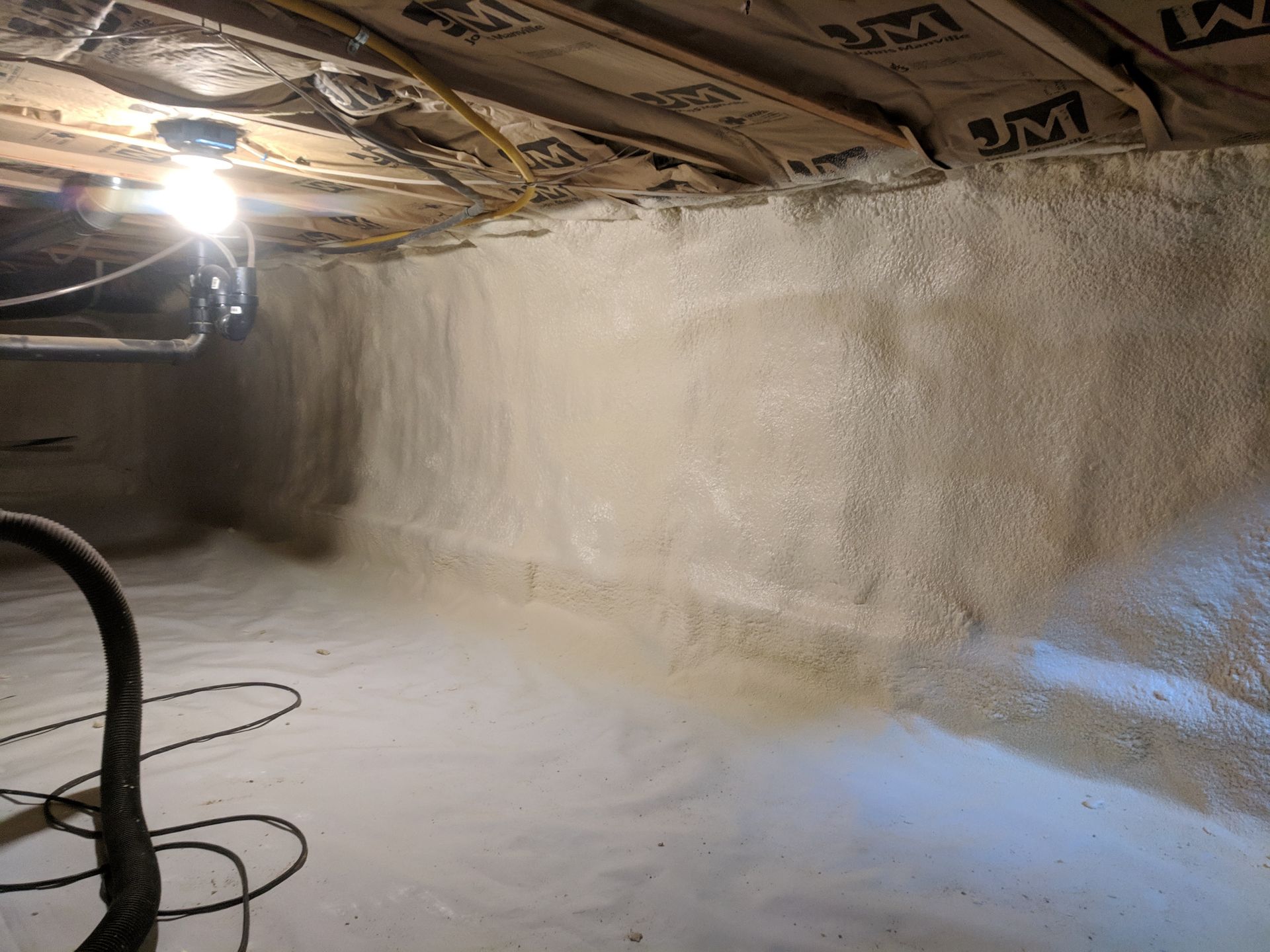 Crawlspace with insulated walls, bare floor, exposed wiring, and a hanging light bulb