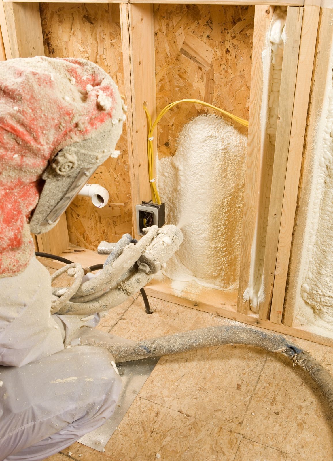 Person spraying foam insulation into a wall cavity with electrical wiring visible.