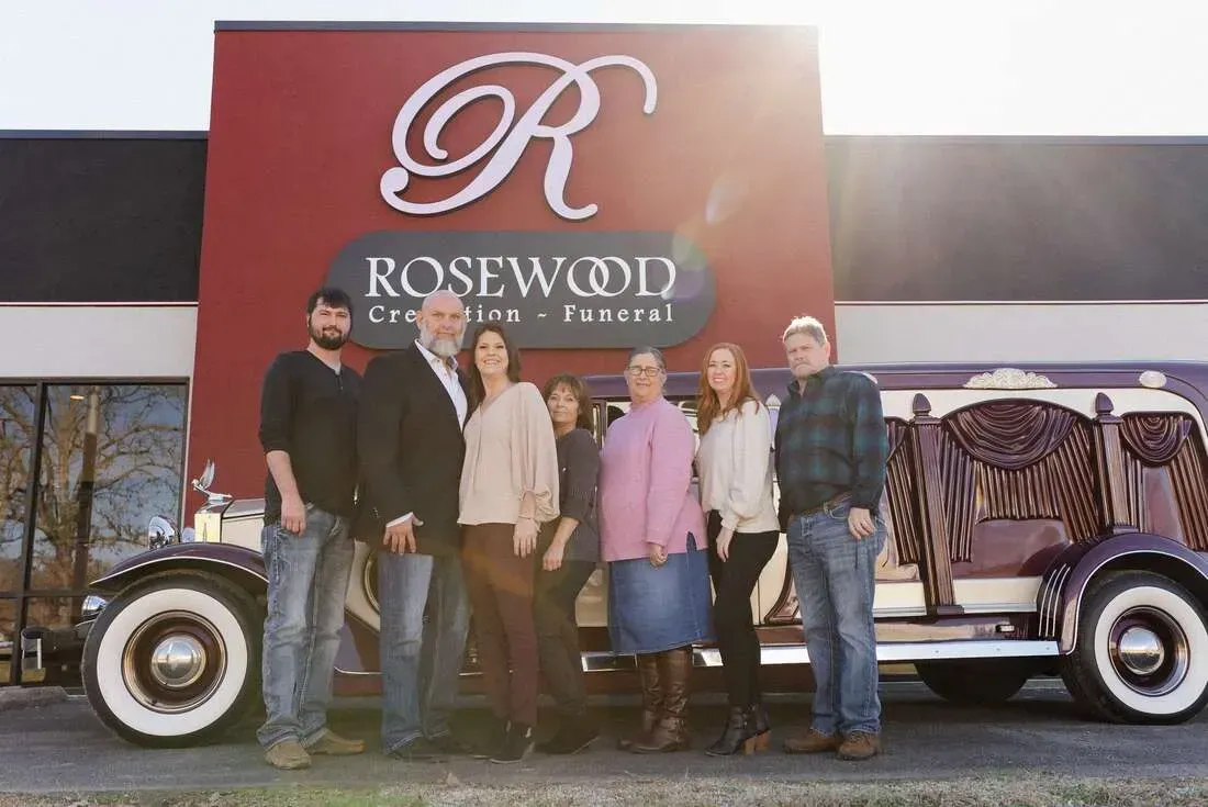 Five people posing in front of a Roswood bus with a large red sign and decorative curtains.