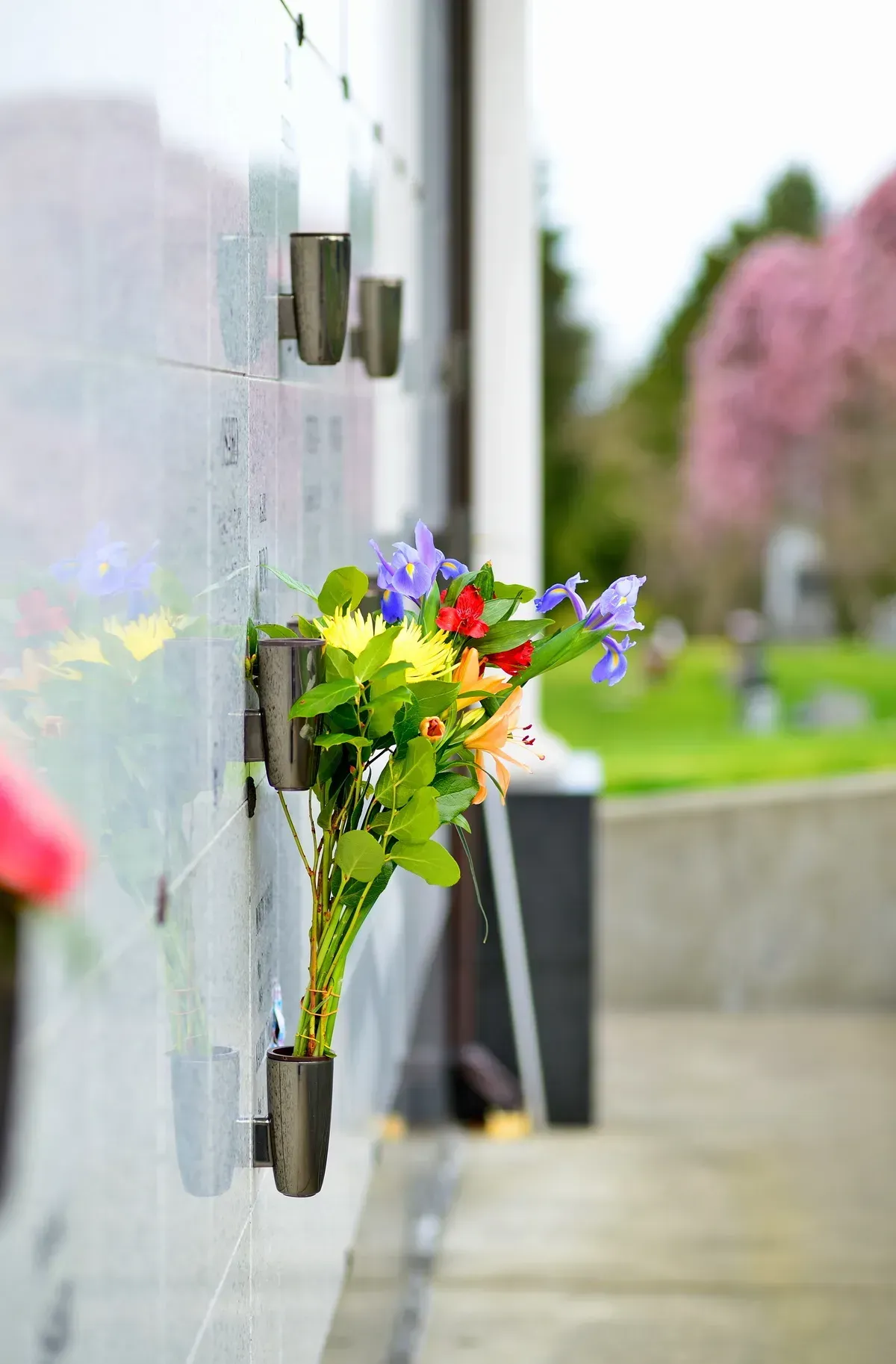 Bouquet of colorful flowers placed in wall-mounted vases along a memorial wall outdoors