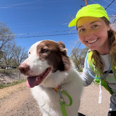 Morgan smiling with dog on leash and path, wearing running gear, lime green hat.