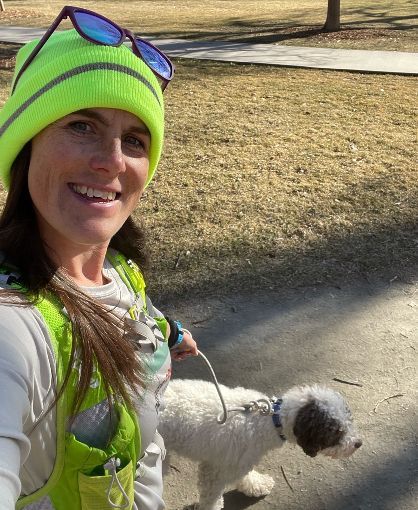 A woman is walking a small dog on a leash in a park.