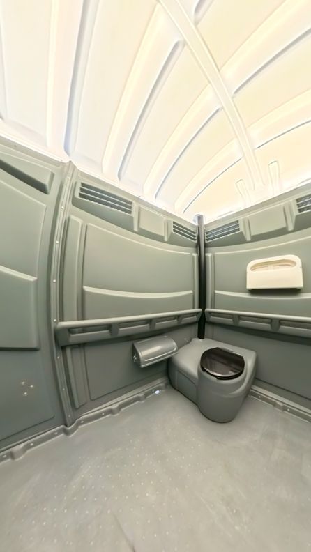 Interior of a gray portable toilet with a toilet seat, hand sanitizer, and ventilation.