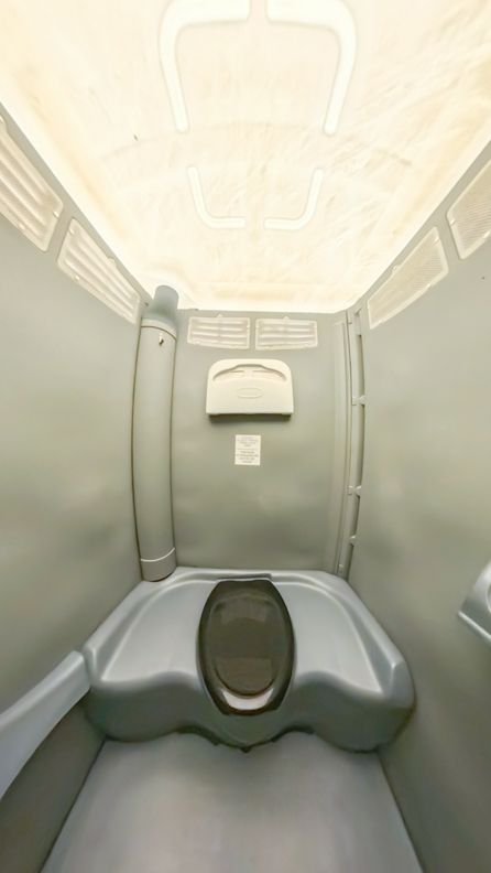 Interior view of a gray portable toilet with the toilet seat and wall-mounted accessories visible.