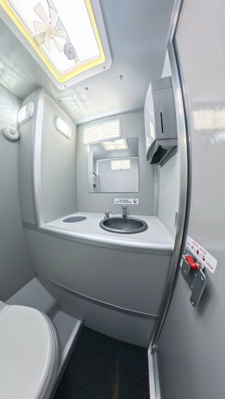 Small, gray airplane bathroom: toilet, sink with mirror, paper towel dispenser.