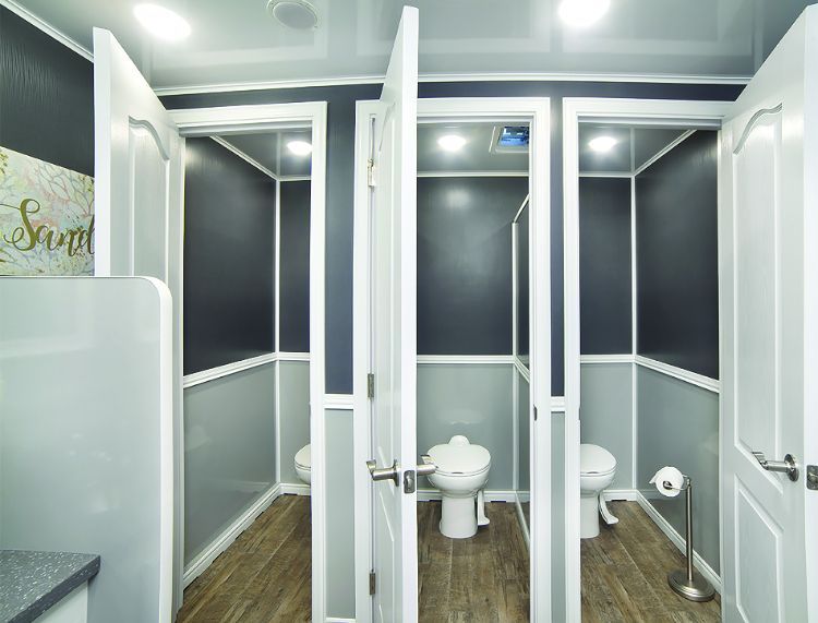 Three stalls in a luxury portable restroom, with white and gray walls, and a wooden floor.