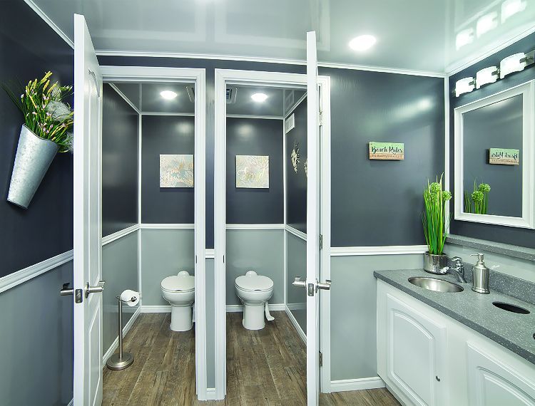 Interior view of a luxury portable restroom with three stalls, gray and white walls, and a sink.