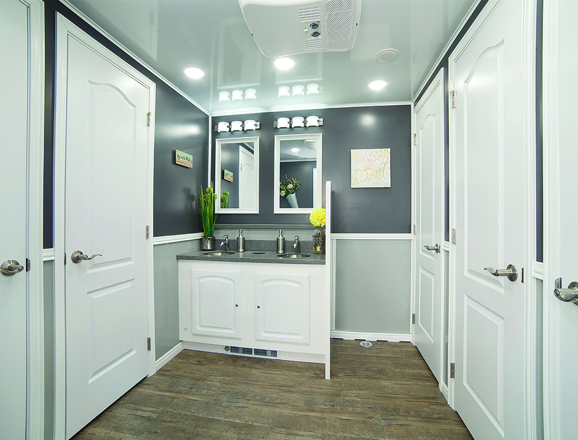 Interior of a luxury portable restroom with white doors, grey walls, and a double sink vanity.