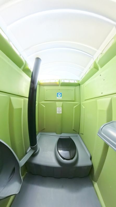 Inside view of a green portable toilet with a toilet seat, a waste pipe, and a hand sanitizer dispenser.