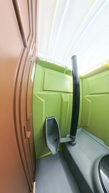 Interior of a portable toilet: green walls, a urinal, and a dark exhaust pipe. Brown door on the left.