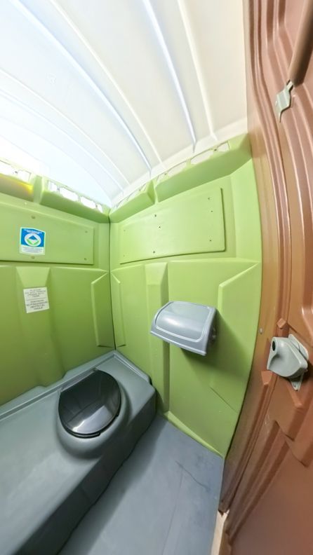 Interior of a green and brown portable toilet, featuring a toilet seat and toilet paper dispenser.