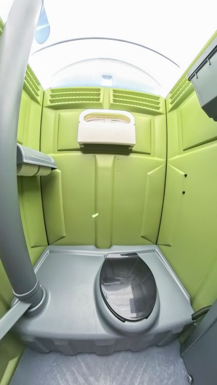 Interior of a green portable toilet. Features include a toilet seat, toilet paper dispenser, and gray floor.