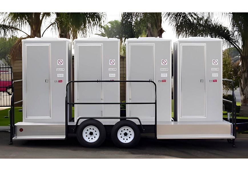 Portable restroom trailer with four stalls; gray, with a black railing and white tires.