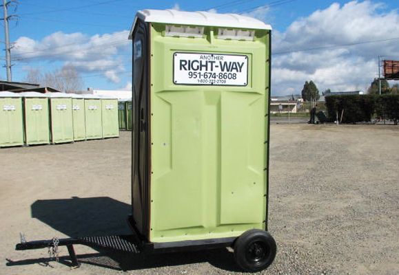 Green portable toilet on wheels, in front of a row of others, outdoors.