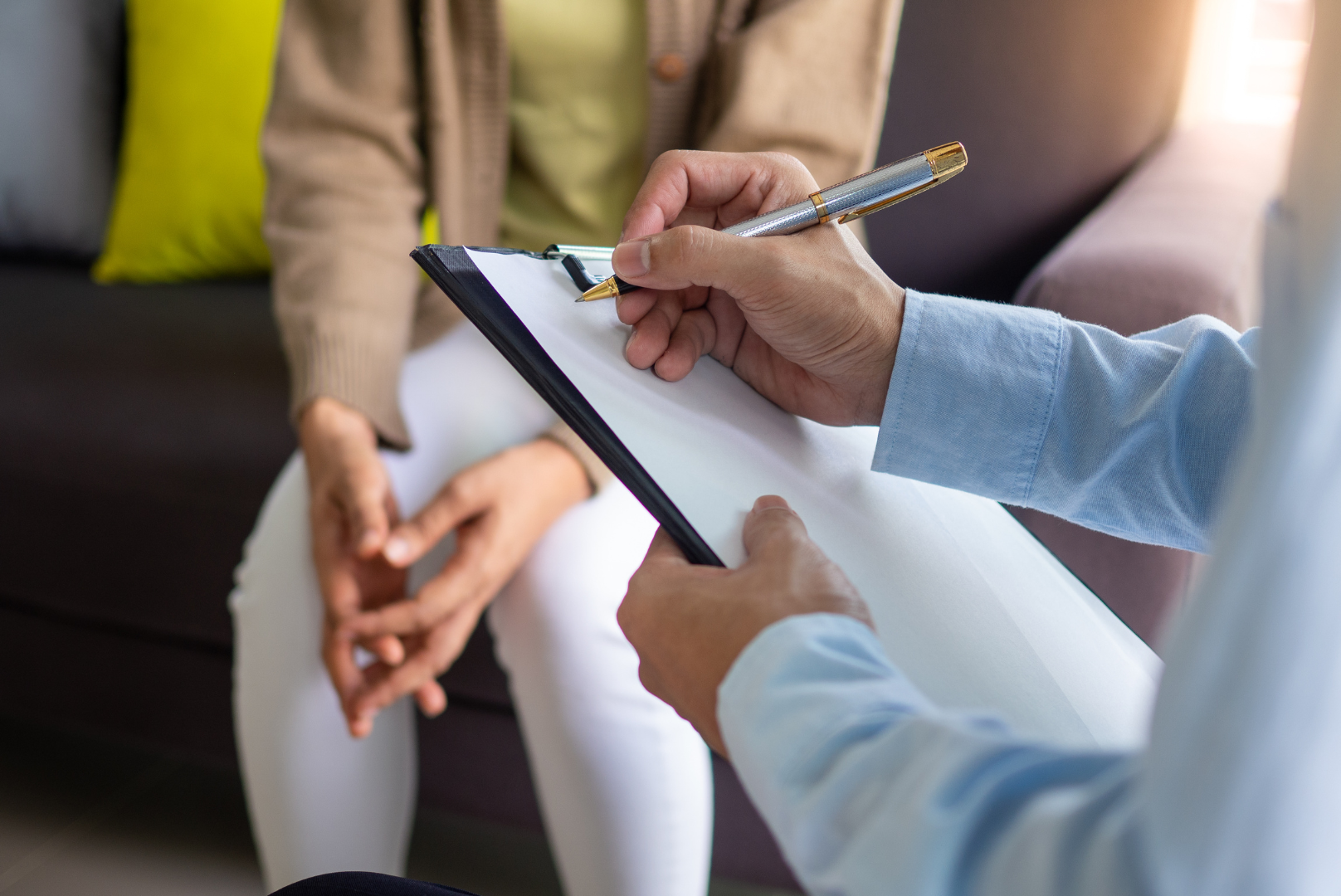 An acupuncture therapist is holding a clipboard and writing during a new client consultation with a client across from him as they conversate