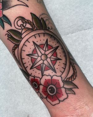 A traditional-style tattoo on a forearm featuring a compass, rope, and red flowers with eye-like centers.