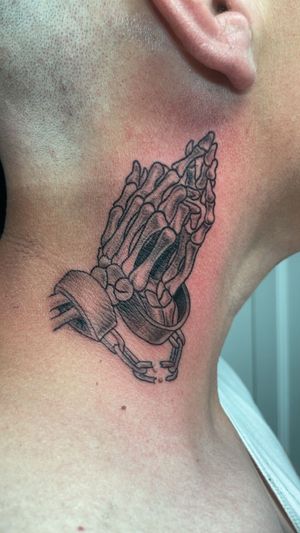 A tattoo on a person's neck depicting two skeleton hands clasped in prayer, with broken handcuffs on the wrists.