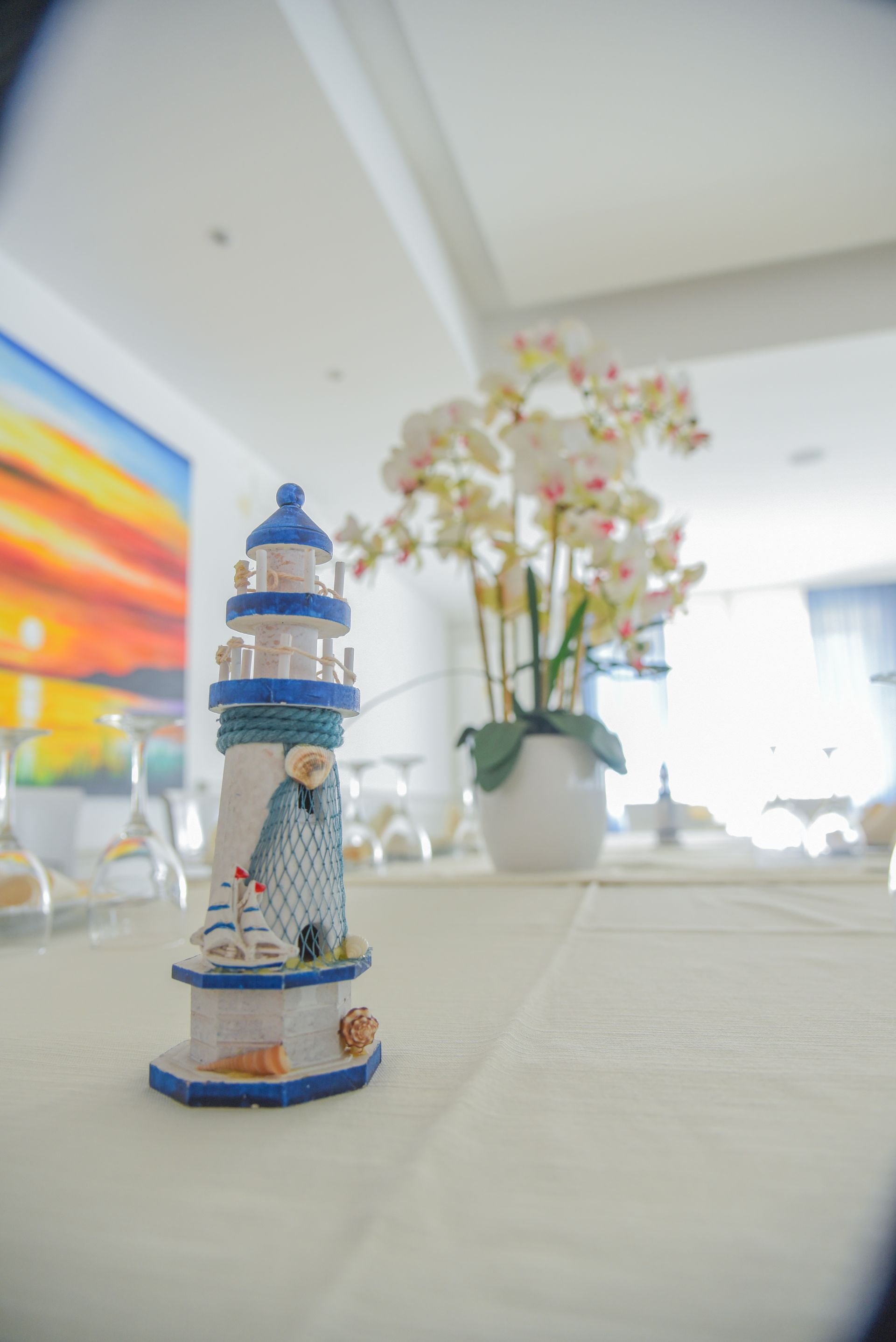 Piccola statuetta decorativa di un faro su un tavolo, con fiori sullo sfondo in una stanza luminosa.