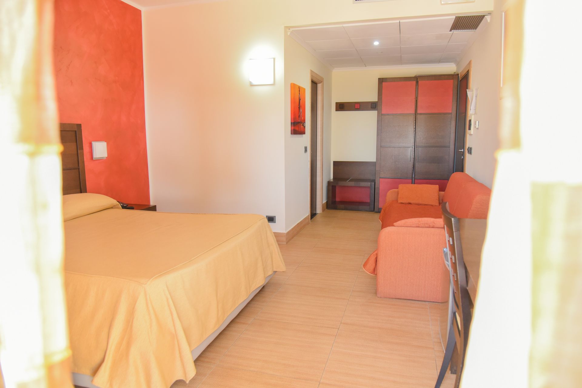 Camera d'albergo compatta con letto, sedie arancioni e un armadio vicino alla porta.