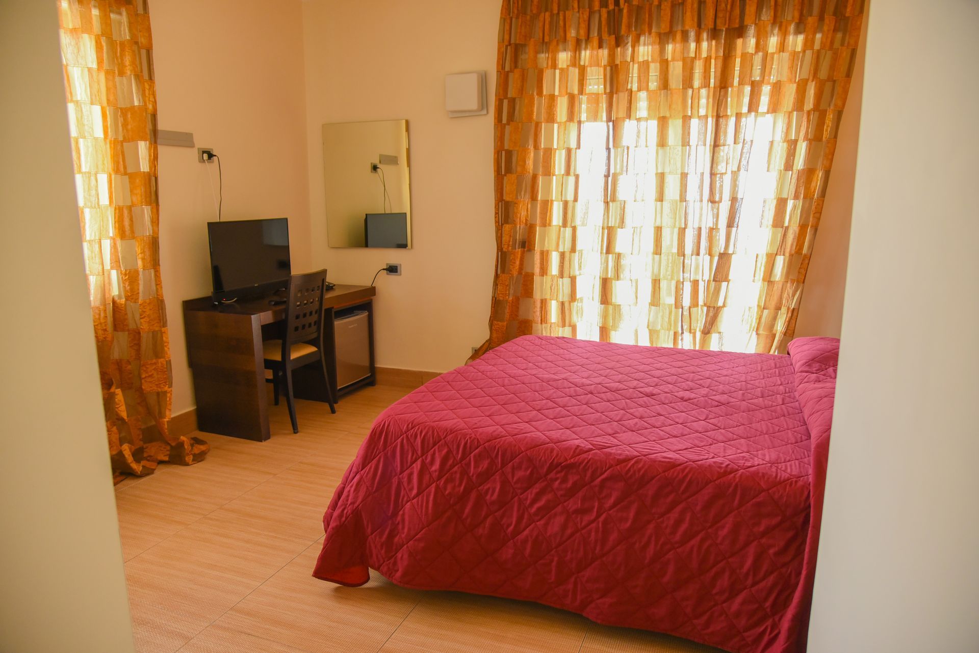 Camera da letto con copriletto rosso, scrivania e tende arancioni in un piccolo appartamento.