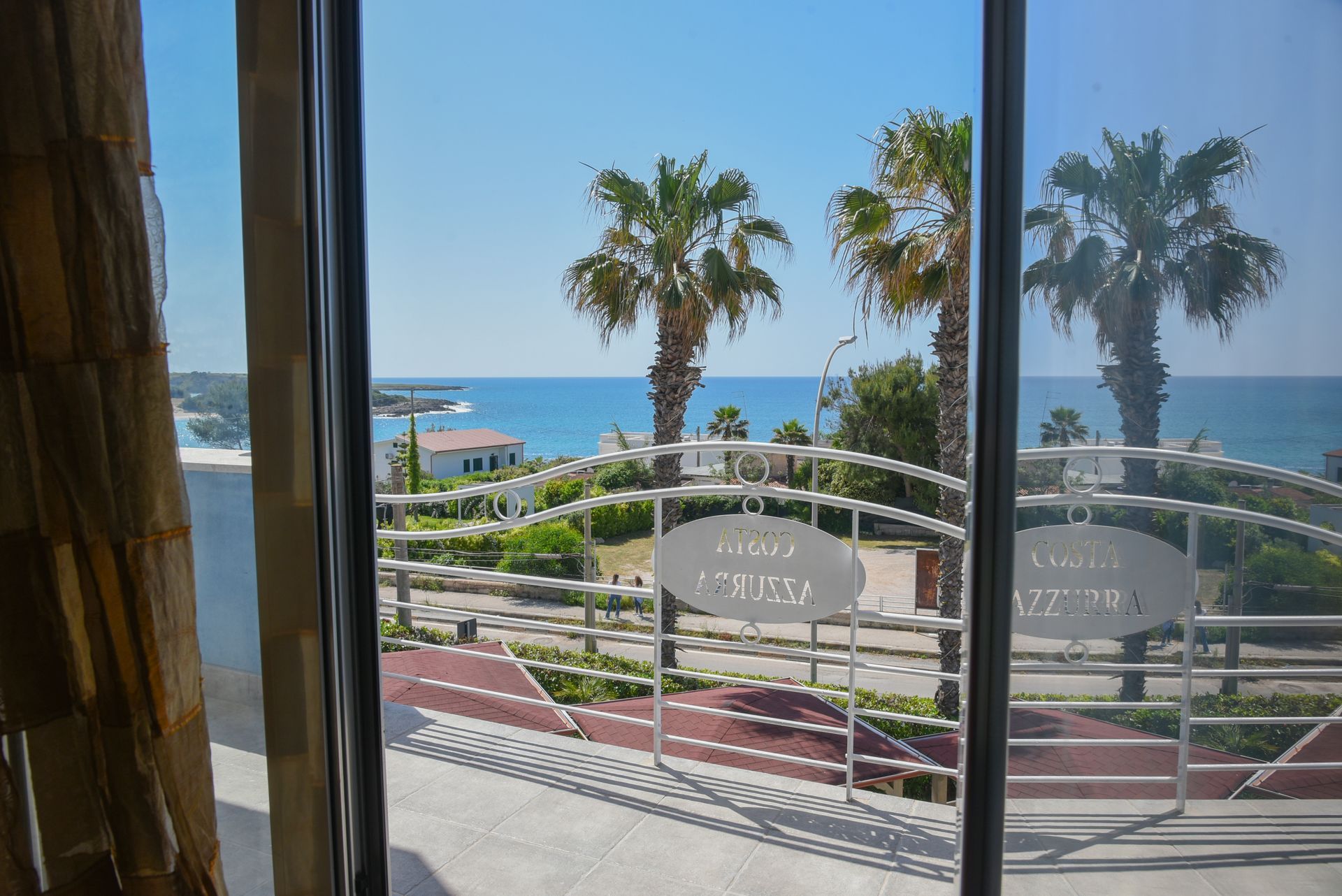 Vista dalla finestra di un resort sul mare con palme, oceano blu e cielo limpido.