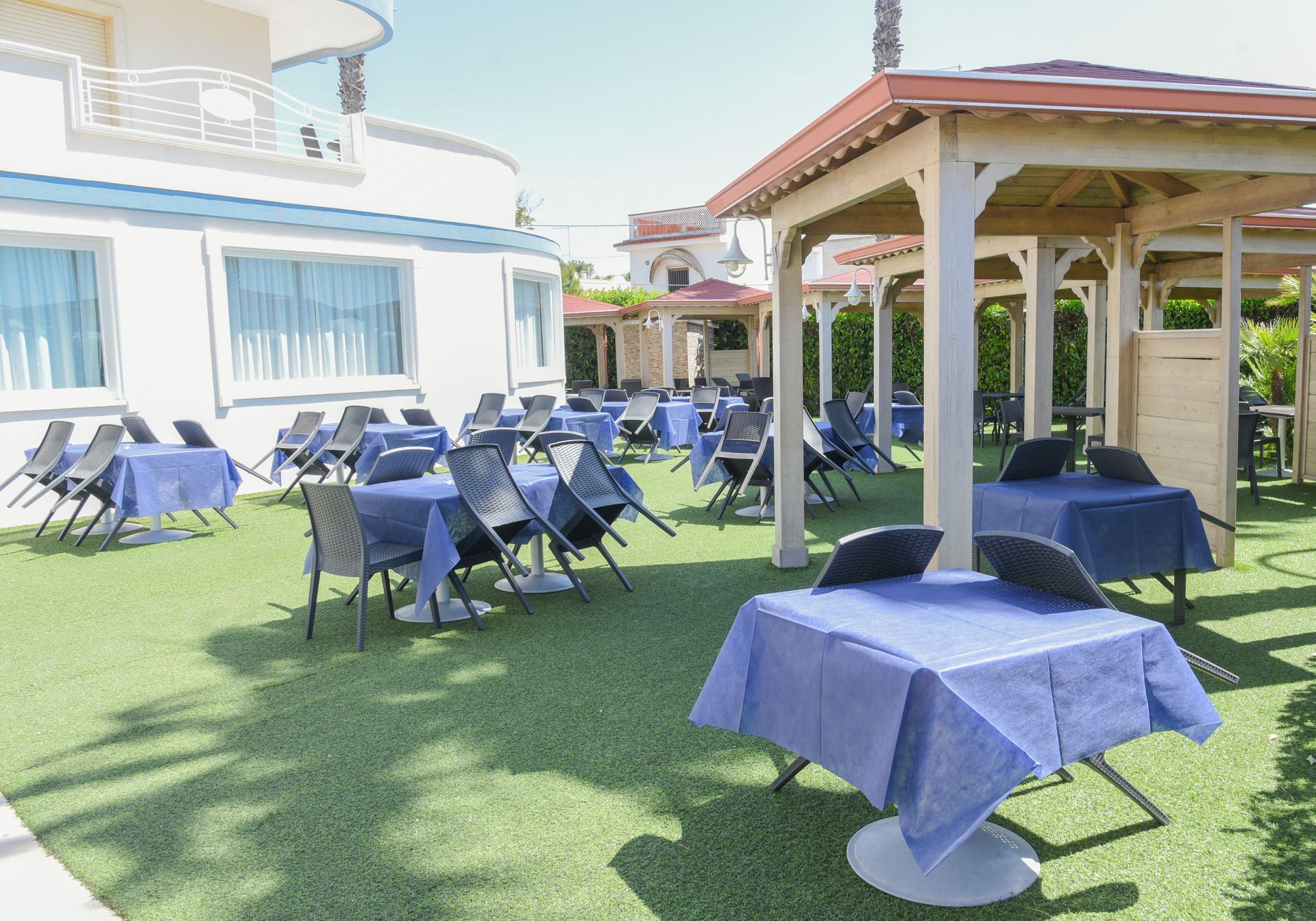 Patio esterno con tavoli e sedie coperti di blu su un prato verde accanto a un edificio
