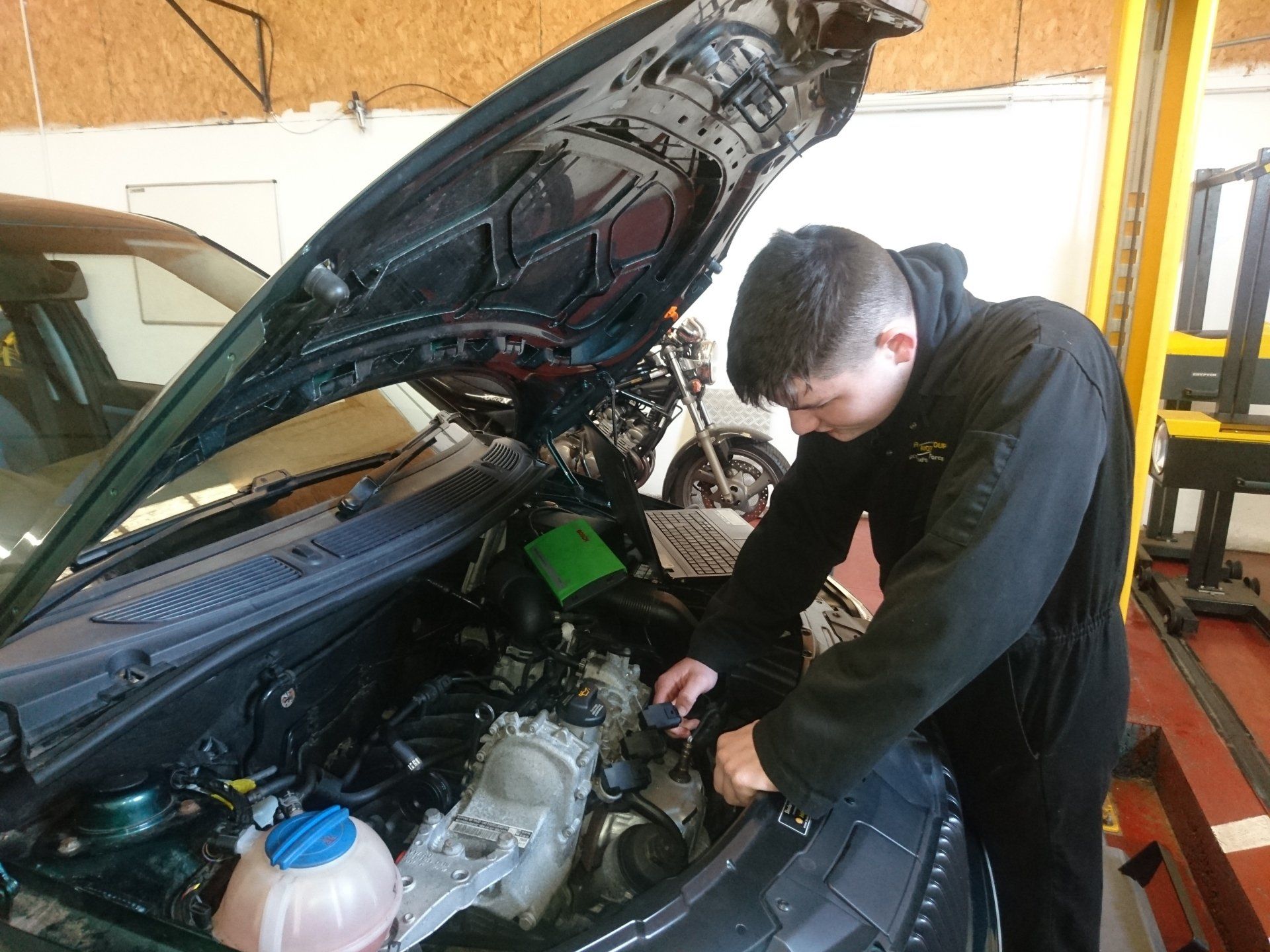 Person working on a car engine in a garage with the hood open.
