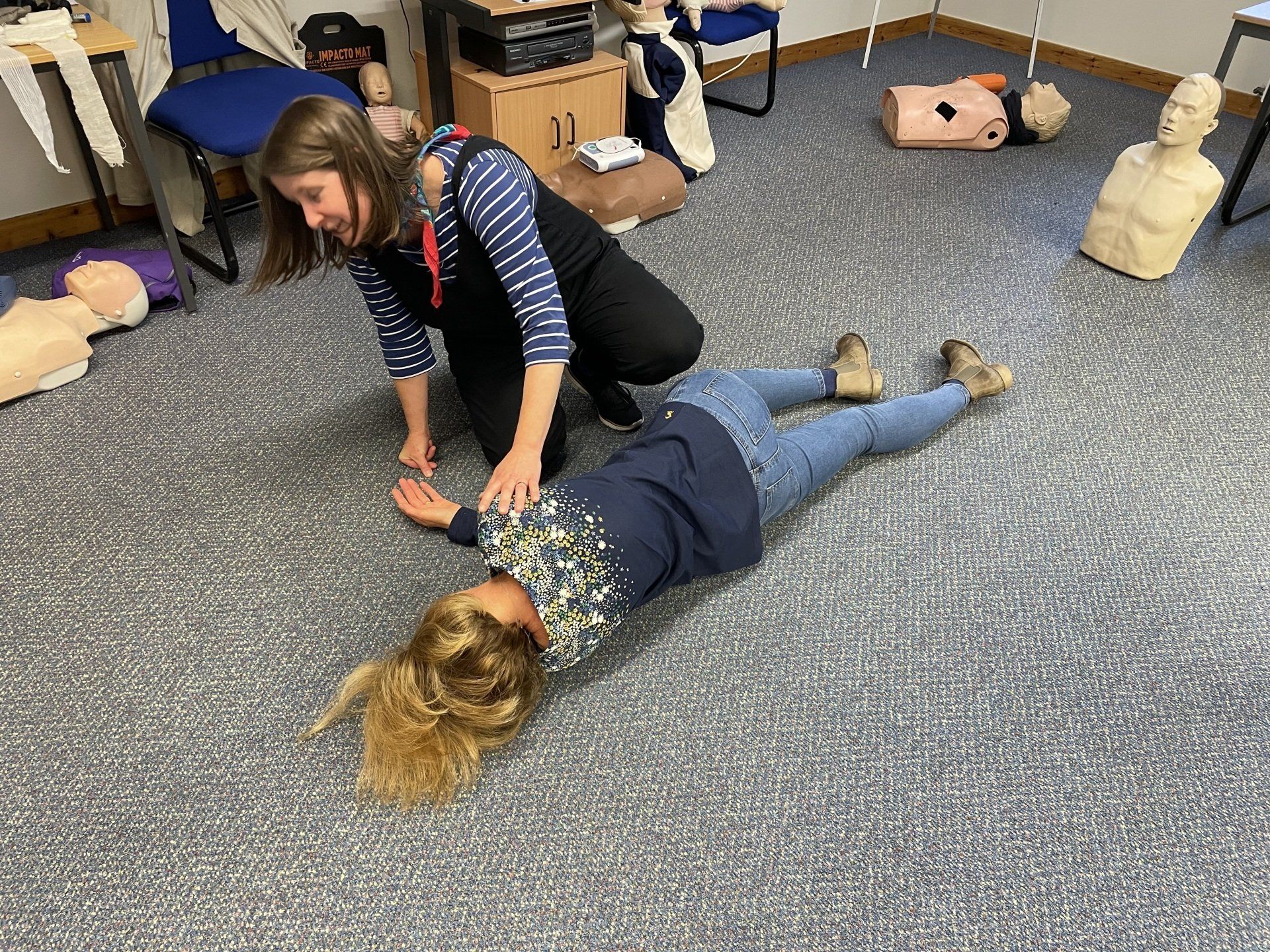 Therapist guiding a child lying on the floor in a classroom, using hands-on exercise with toys nearby