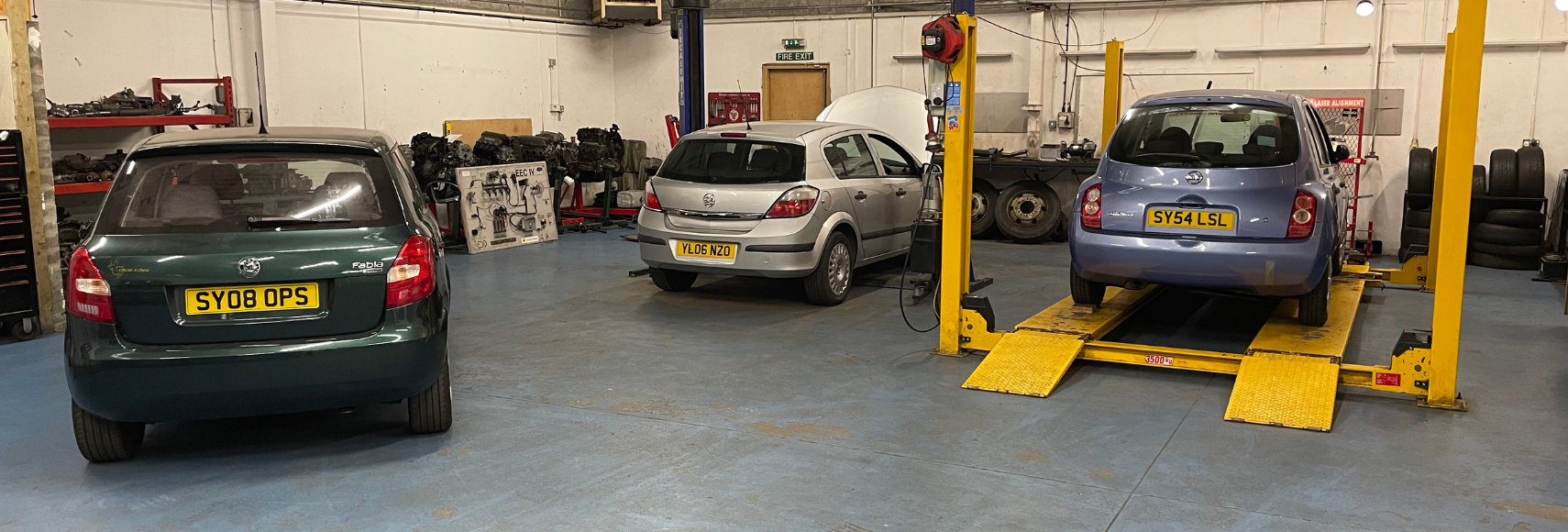 Car repair garage with three cars, including one on a lift and others parked indoors