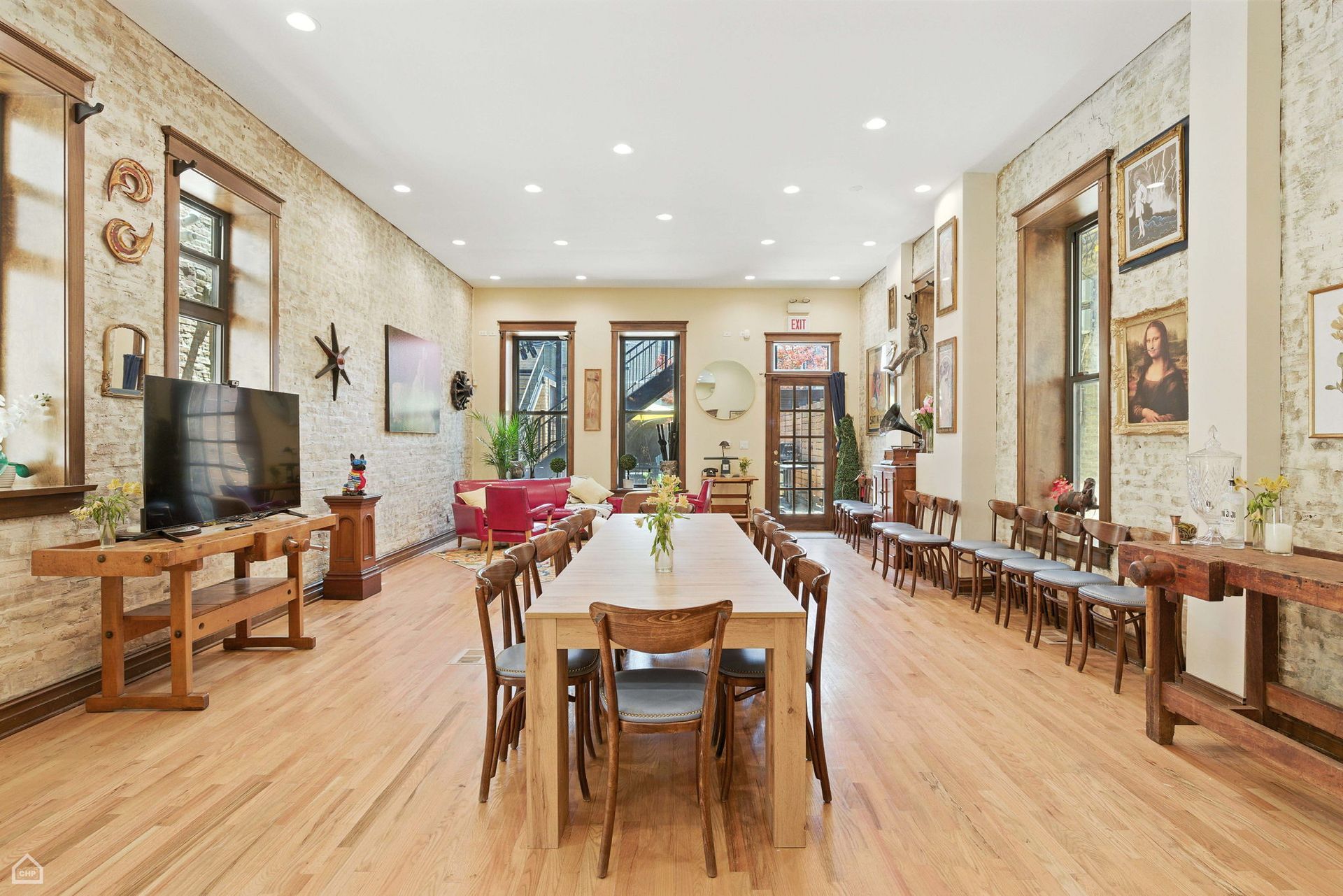 Long dining room with long wooden table, chairs, art, windows, and light wood flooring.