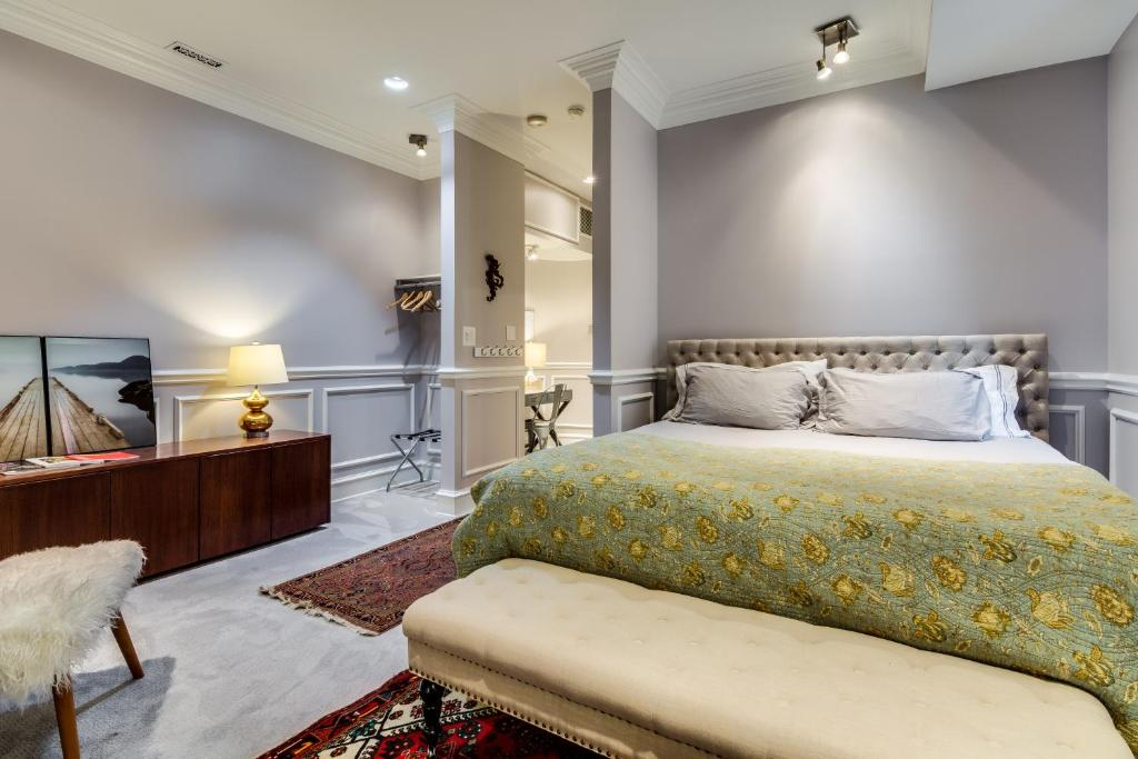 Bedroom with large bed, patterned blanket, bench, and wooden dresser with art.