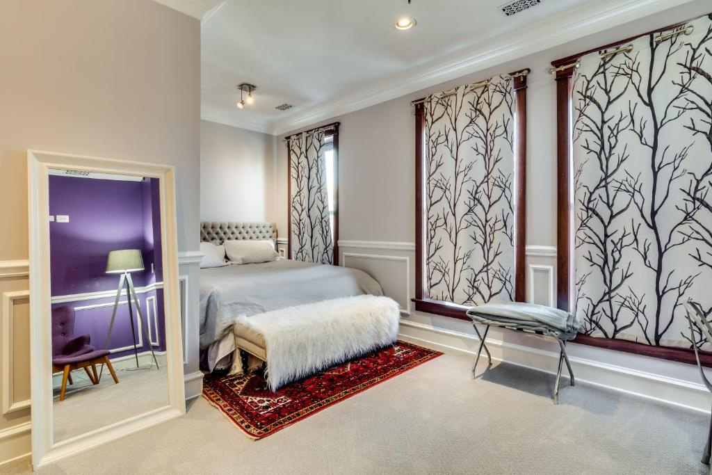 Bedroom with large mirror, bed, bench, patterned curtains, red rug, and gray walls.