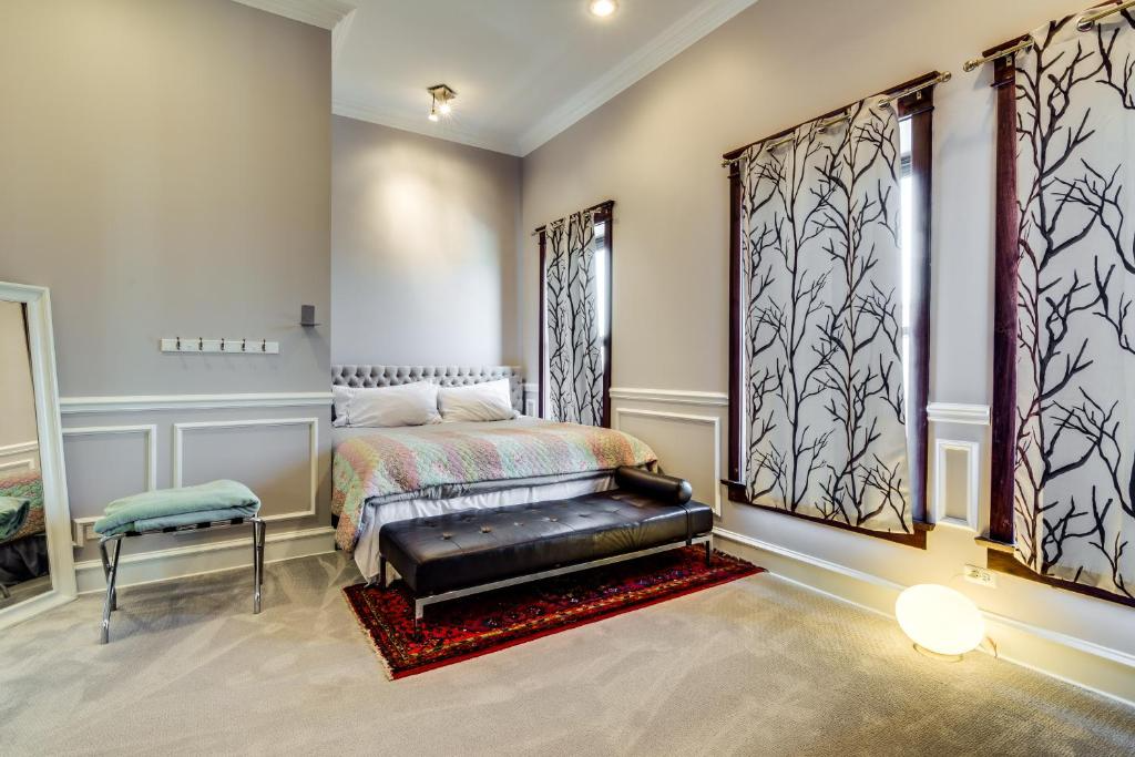 Bedroom with bed, bench, patterned curtains, and mirror. Gray walls, rug, and soft lighting.